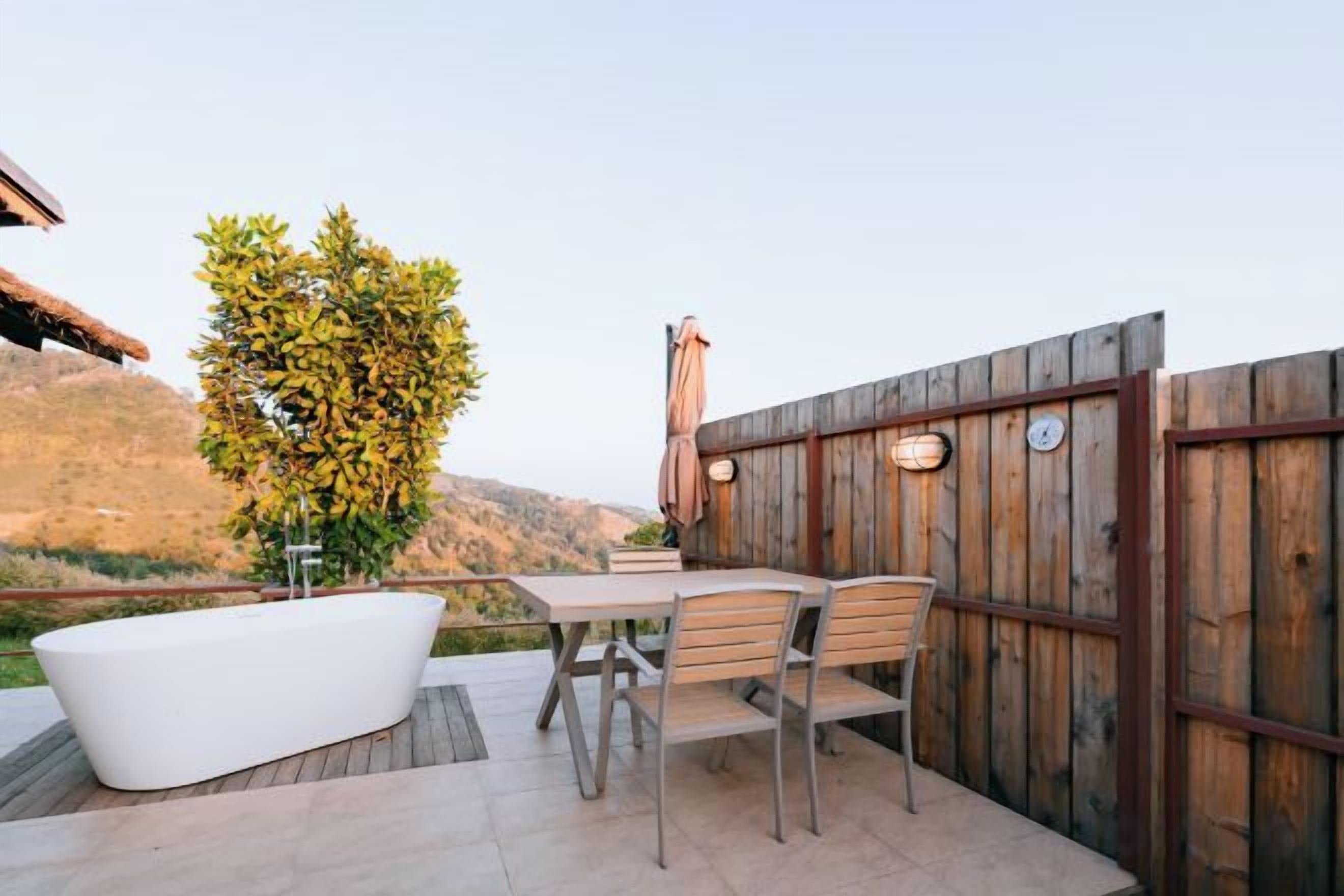 Un patio exterior con una bañera blanca, una mesa de madera y sillas.