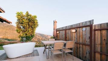 Un patio exterior con una bañera blanca, una mesa de madera y sillas.