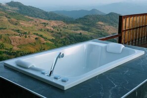 A modern bathroom with a large bathtub, a wooden chair, and a view of rolling hills.