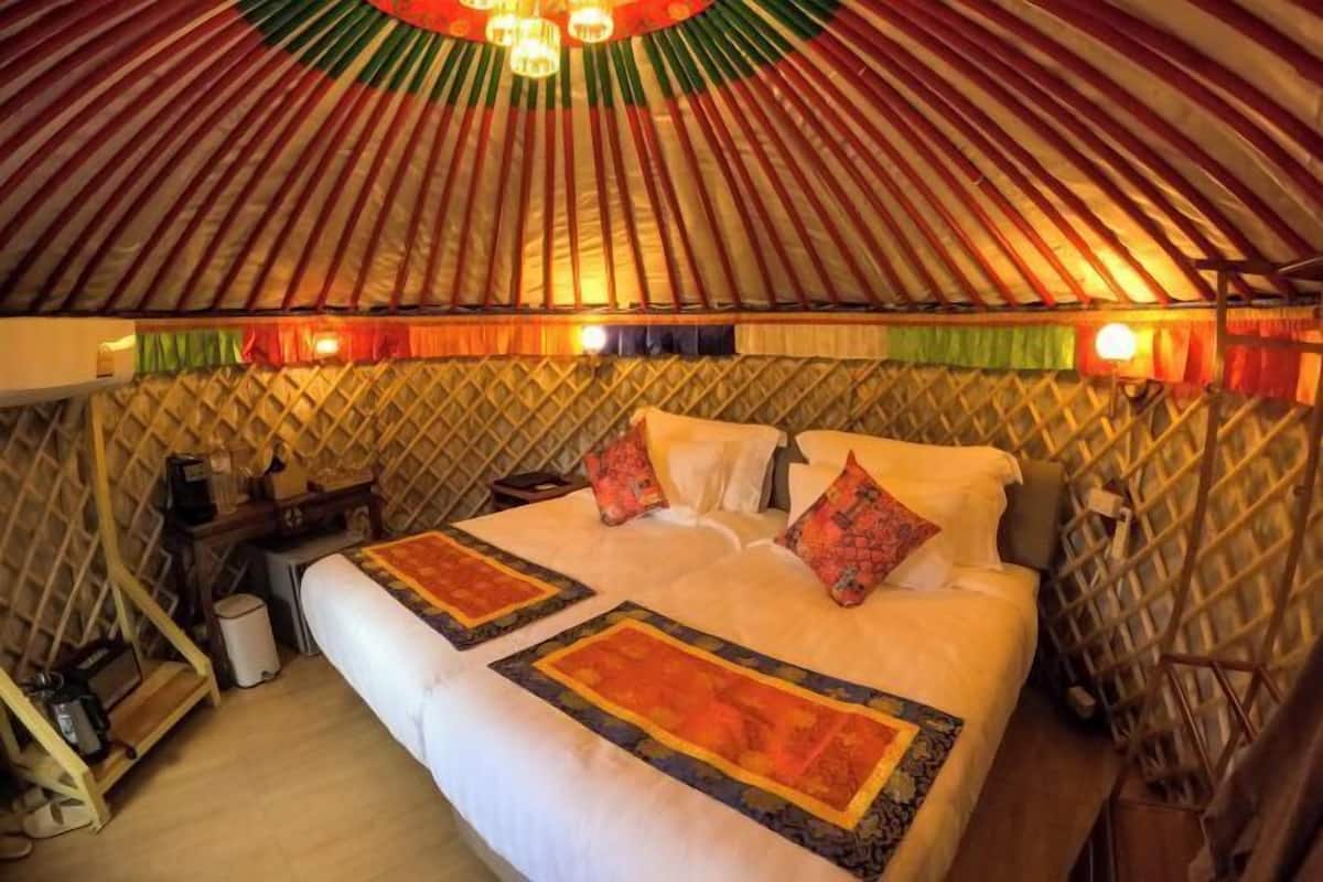 A traditional yurt interior with a bed, pillows, and a small table with a lamp.