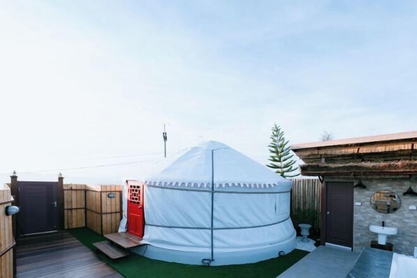 Une yourte dotée d’une terrasse en bois, d’une porte rouge et d’un petit espace jardin agrémenté d’un tapis vert.