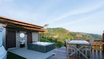 Una terraza con hidromasaje, mobiliario exterior y vistas a un paisaje montañoso.