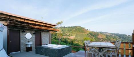 A deck with a hot tub, outdoor seating, and a view of a hilly landscape.
