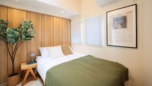A bedroom with a bed, a nightstand, a potted plant, and a wall-mounted air conditioner. - Infinity Grove in Ikebukuro・ZHUOJU (Tokyo)