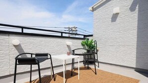 An outdoor patio with a white table and two black chairs, a small potted plant, and a brown rug. - Infinity Grove in Ikebukuro・ZHUOJU (Tokyo)