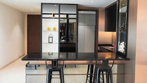Une cuisine moderne avec un plan de travail noir, deux tabourets de bar et un réfrigérateur encastré.