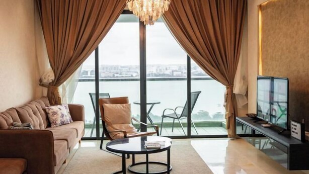 Un salon moderne avec un canapé, une table basse ronde et un téléviseur. De grandes fenêtres offrent une vue sur un plan d’eau et sur le paysage urbain.