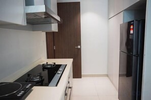A compact kitchen with a stove, oven, and a refrigerator. - The Marina View Johor Bahru (Plentong)