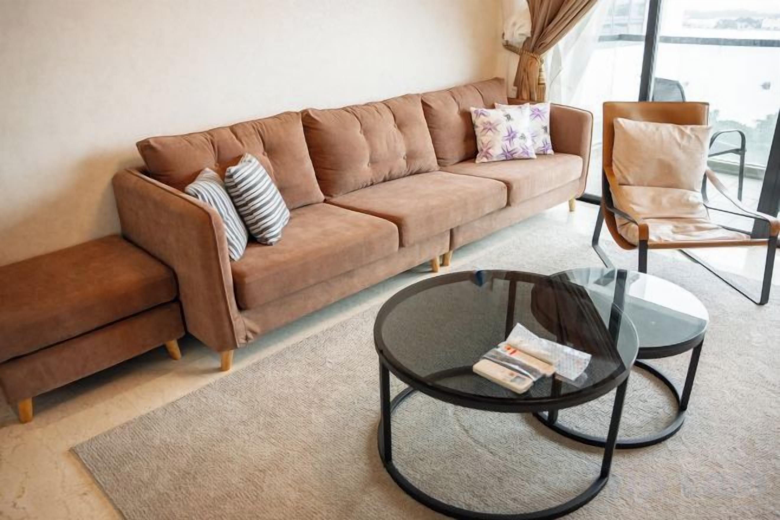 A brown sofa with striped and floral pillows, a round glass coffee table, and a chair with a cushion.