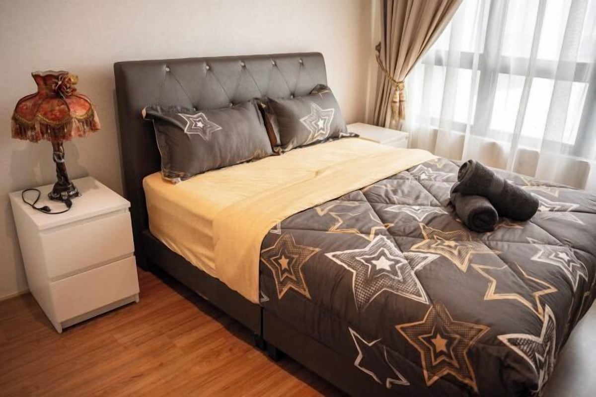 Une chambre à coucher avec une tête de lit capitonnée, un lit recouvert d’une couette à motifs étoilés, une lampe de chevet et une table de chevet blanche.