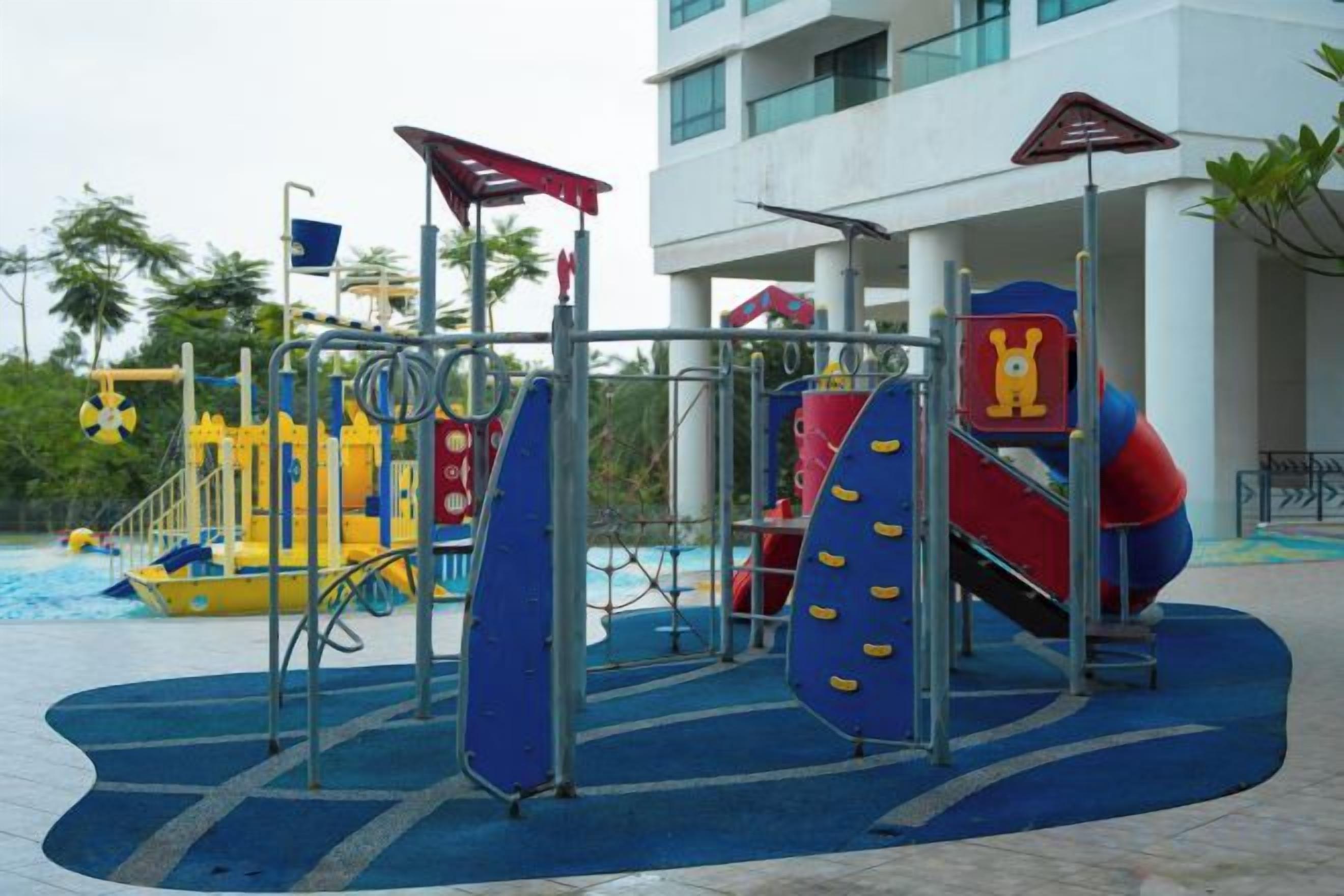 A playground with slides and climbing structures, located in an outdoor area with a building in the background.