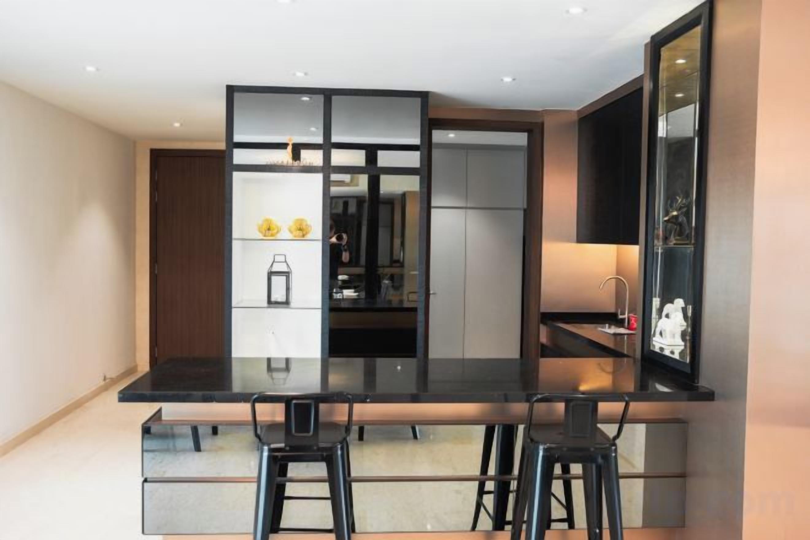 A modern kitchen with a black countertop, two bar stools, and a built-in refrigerator.