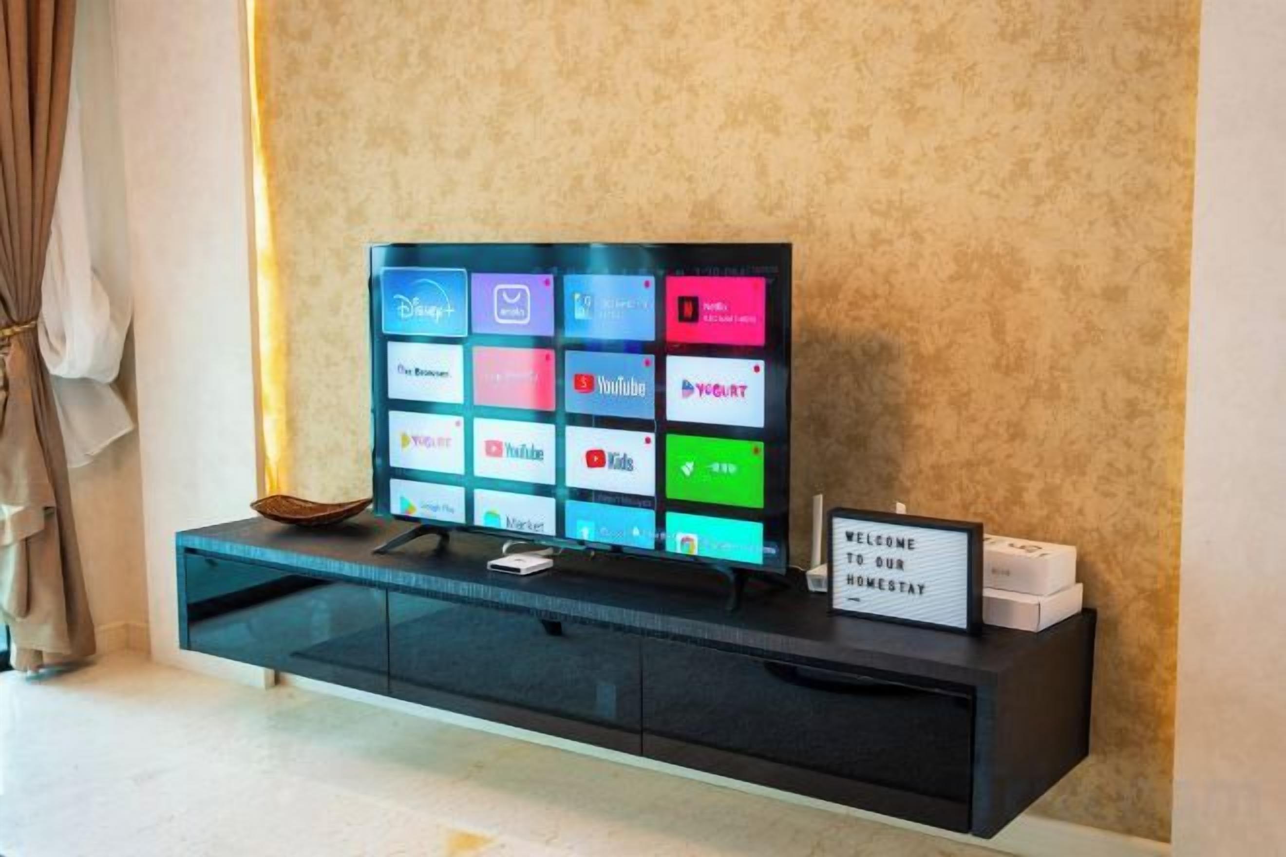 Ein Flachbildfernseher auf einer schwarzen Unterhaltungsecke mit einem Schild, auf dem 'WILLKOMMEN IN UNSEREM HOTEL' steht.