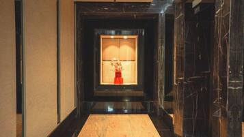 Un pasillo con piso de mármol que conduce a una habitación con un gran ventanal y un jarrón rojo.
