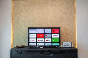Et fladskærms-tv med en række app-ikoner på et sort stativ foran en væg med struktur.