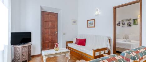 A cozy living room with a sofa, a television, a wooden door, and a small table with a vase.