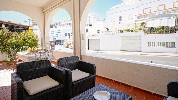 A balcony with wicker furniture, a table with a glass top, and a view of a white building with balconies. - #341 Casa da Guida | Central & Cozy (Albufeira)