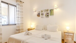A hotel room with two beds, a window with curtains, wall-mounted artwork, and bedside lamps. - #341 Casa da Guida | Central & Cozy (Albufeira)