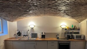 A compact kitchen with a wooden countertop, a sink, a stove, and a microwave. There are two wall-mounted lights and a window on the left. - Stylish apartment in Hamburg-Uhlenhorst (Hamburg)
