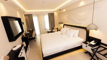 A modern hotel room with a large bed, bedside table with a lamp, a desk with a chair, and a television on the wall.