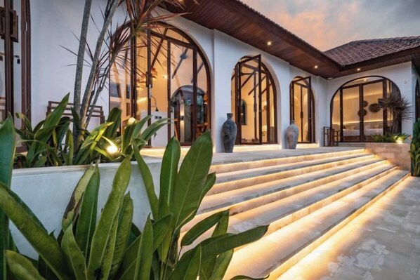 Una casa moderna con una escalera de piedra que conduce a una puerta de cristal, rodeada de follaje.