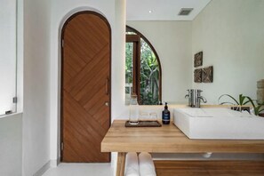 Une salle de bain moderne avec une porte en bois, un grand miroir, un lavabo blanc et un plan de toilette en bois.
