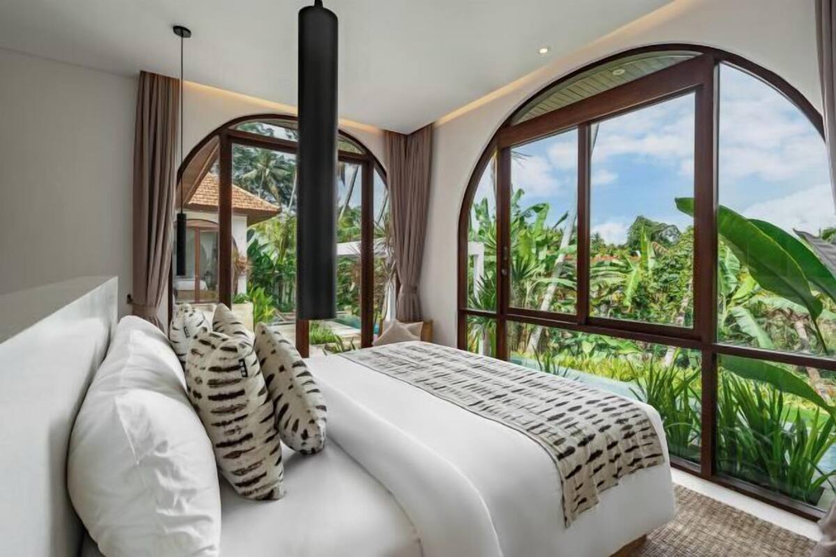 Een slaapkamer met een groot bed, uitzicht op weelderige begroeiing en een gebogen raam.