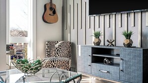 A modern living room with a glass table, a leopard print chair, a guitar, a TV, and decorative plants. - Harmony House #6–Roomy Retreat–Sleeps 12 (Nashville)