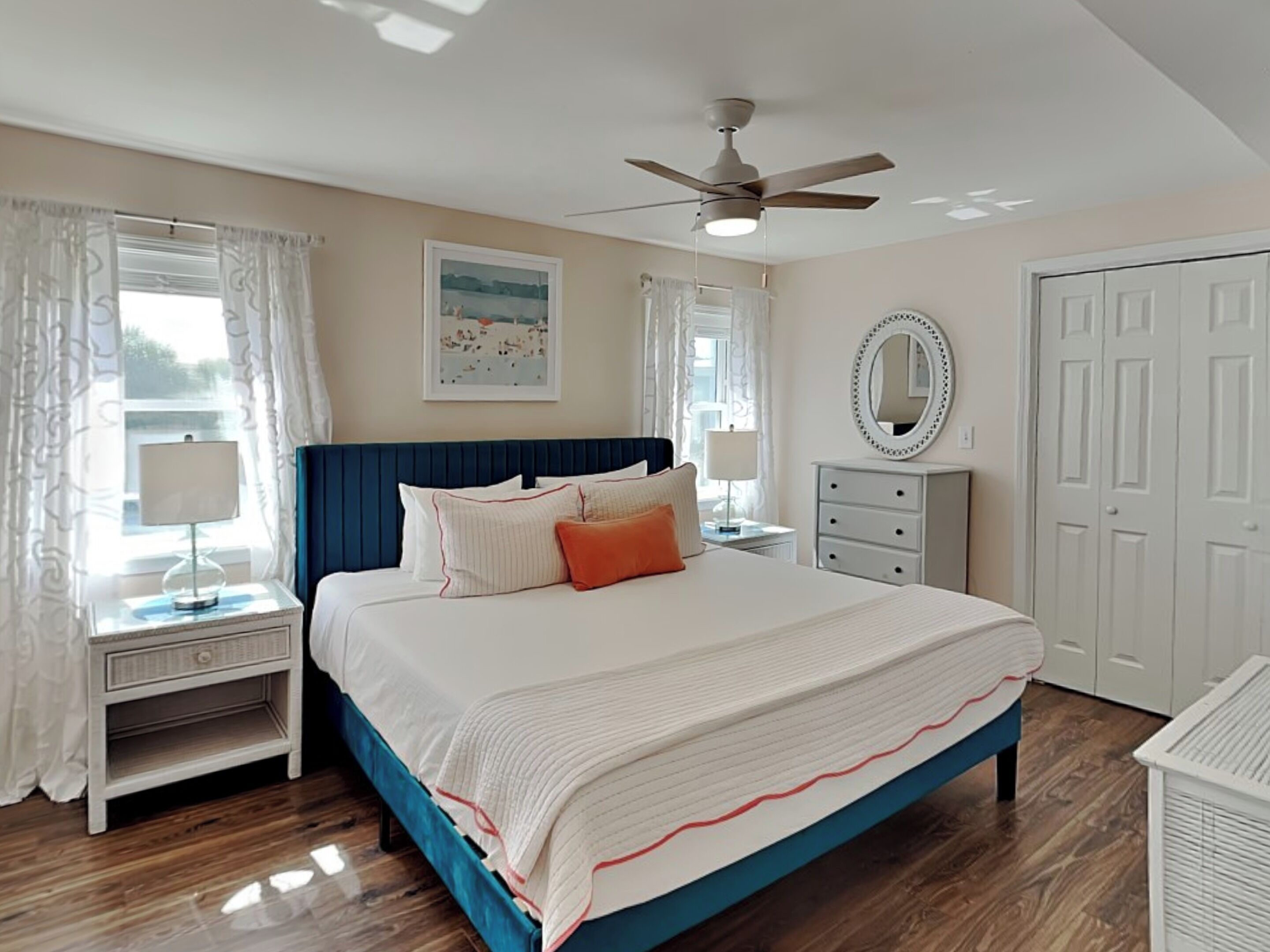 A bedroom with a bed, a nightstand, a dresser, a ceiling fan, and a window with curtains.