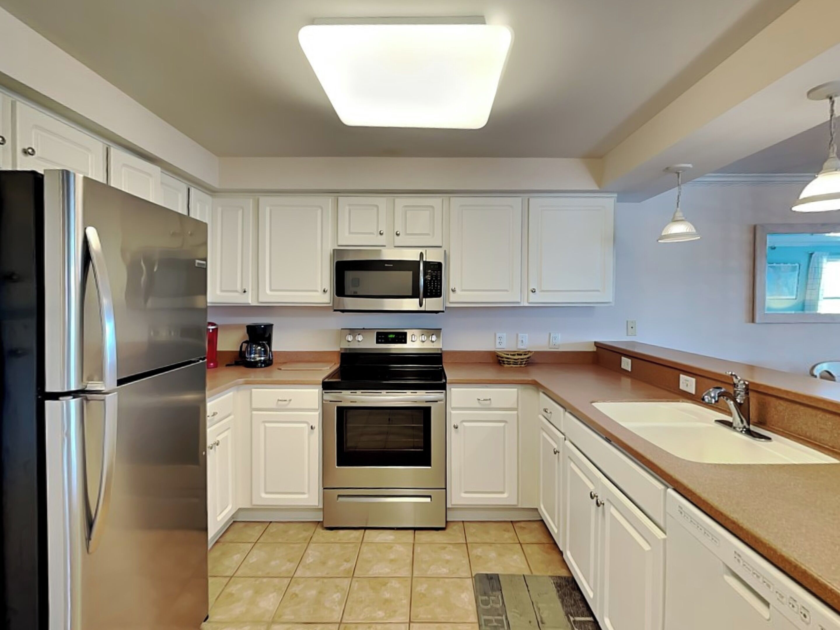 A modern kitchen with white cabinets, stainless steel appliances, and a tiled floor.
