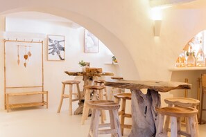 Un intérieur rustique avec une table et des tabourets en bois, des œuvres d’art encadrées accrochées aux murs et une décoration suspendue.