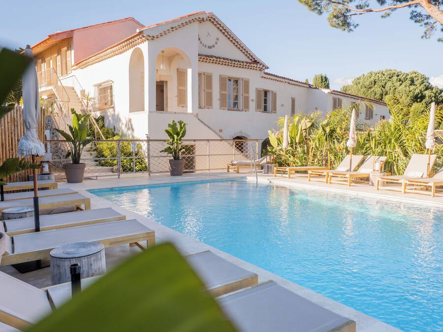 Un área de piscina con sillones de descanso y plantas en macetas.