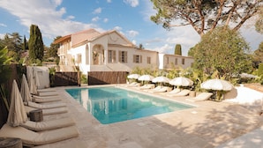 A pool area with lounge chairs and umbrellas, a white building with a tiled roof, and a clear blue sky. - Auberge Tao (Biot)