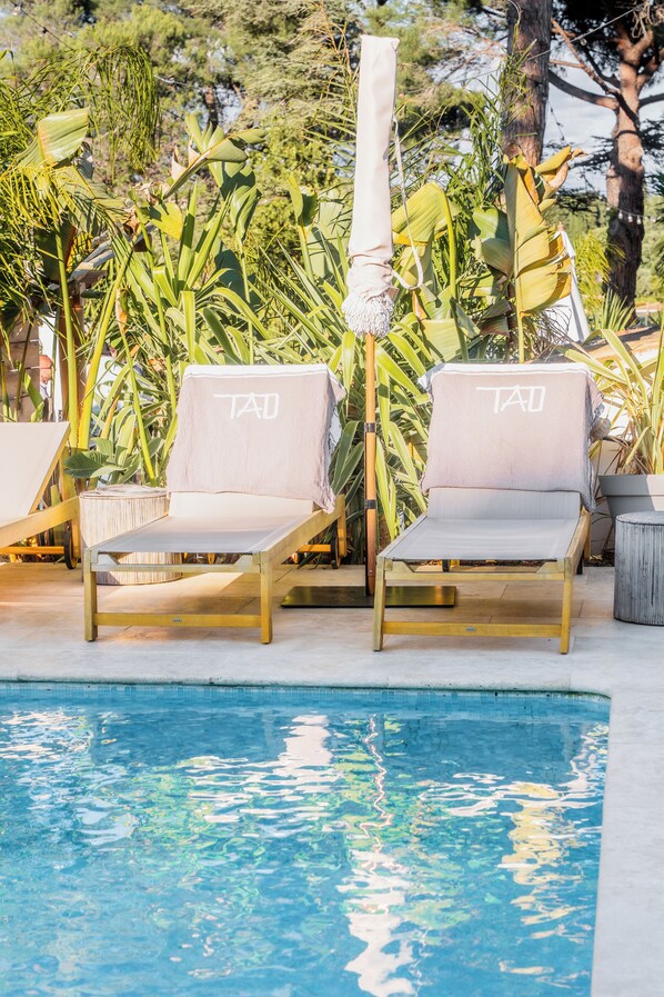 Two lounge chairs with 'TAD' branding, a pool, and tropical foliage in the background. - Auberge Tao (Biot)