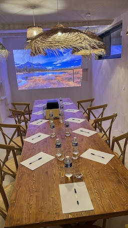 A conference room with a wooden table, chairs, water bottles, pens, and a projector screen displaying a landscape.. Auberge Tao