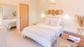 A bedroom with a large bed, wooden headboard, and a round wooden table with a remote control. - Auberge Tao (Biot)
