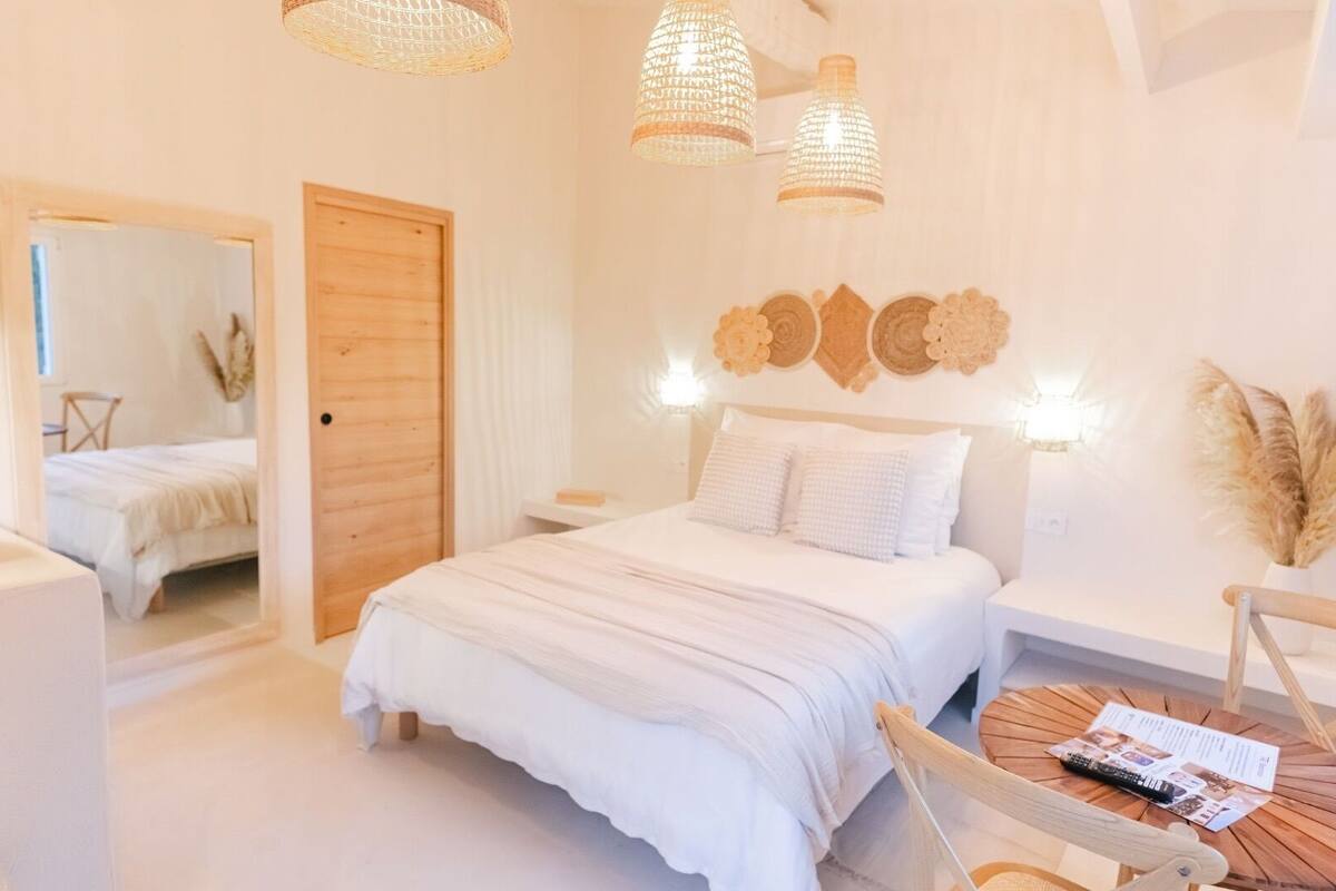 A bedroom with a large bed, wooden headboard, and a round wooden table with a remote control.