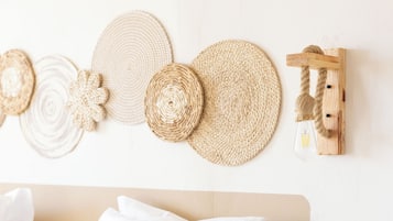 Un lit avec une literie blanche et un oreiller beige, un mur orné d’une décoration murale tissée, et un luminaire en bois fixé au mur.