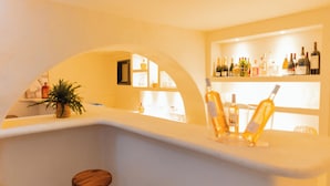 A bar area with a white counter, two wooden stools, and shelves with bottles. - Auberge Tao (Biot)