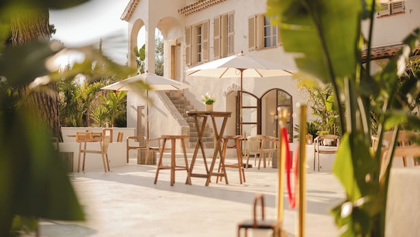 A white building with a tiled roof, outdoor seating with umbrellas, and a staircase leading to an upper level. - Auberge Tao (Biot)