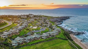 A coastal resort with multiple-story buildings, a parking area, and a view of the ocean.