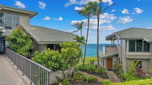 A coastal property with a view of the ocean, featuring modern architecture, a balcony, and lush landscaping.