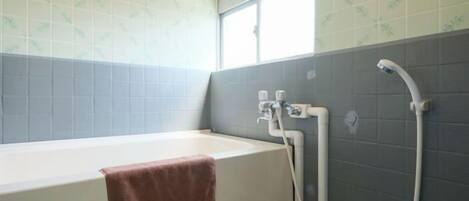 A bathroom with a bathtub, a towel, and a shower area.