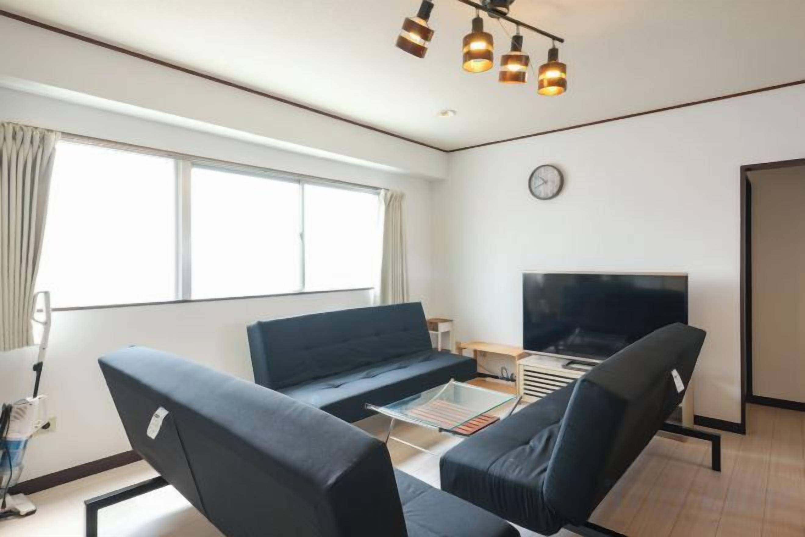 Un salon moderne comprenant un canapé, des fauteuils, une table basse, un téléviseur à écran plat et une grande fenêtre.