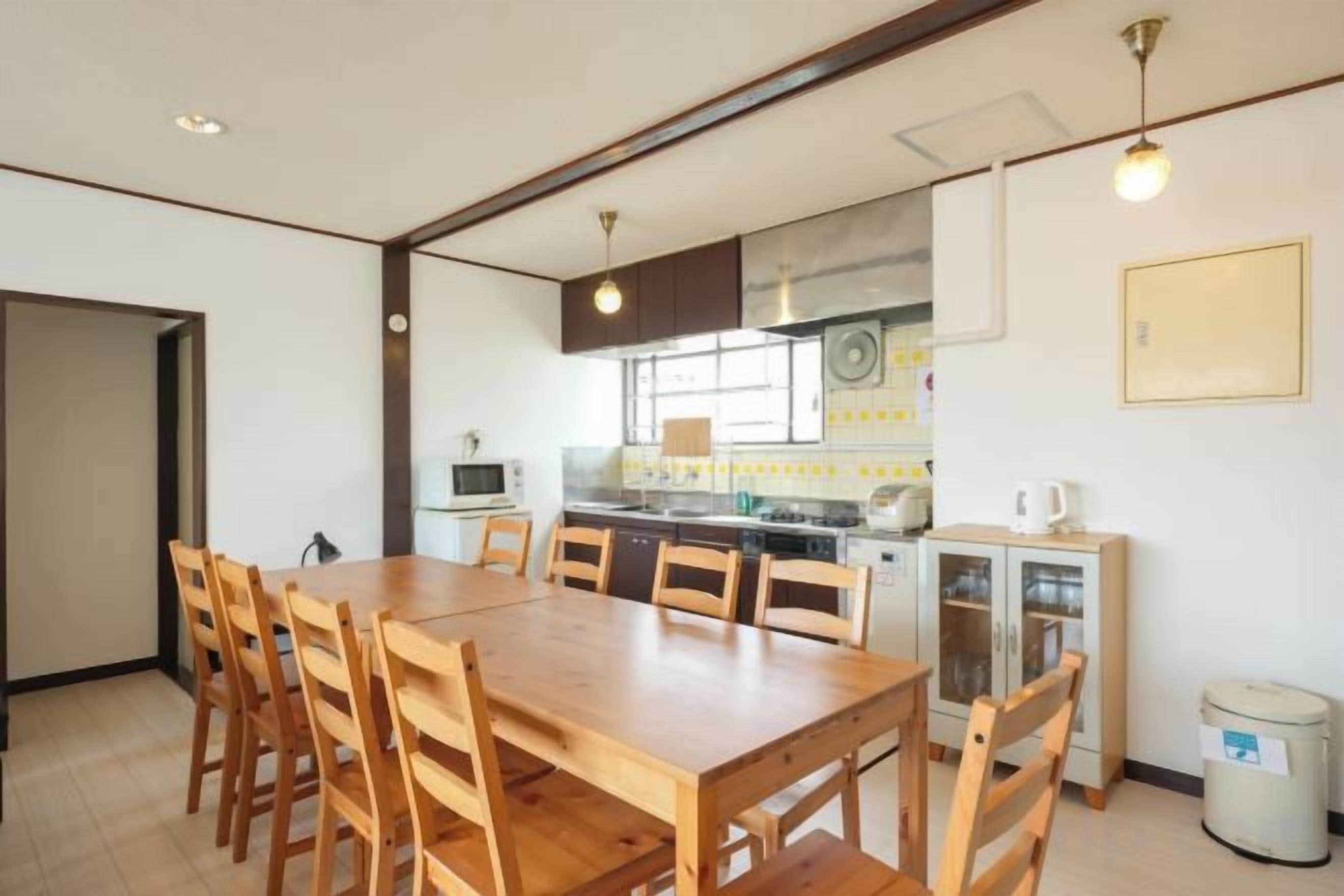 A dining area with a wooden table and chairs, a kitchen in the background, and a trash can.