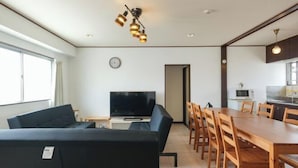 A modern living room with a sofa, TV, dining table, and chairs. - Grace Mukojima Room 701 (Tokyo)