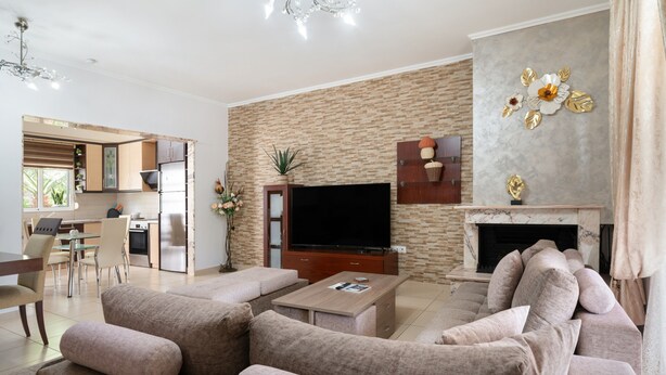 Een moderne woonkamer met een zithoek, een flatscreen televisie, een open haard en een keuken die zichtbaar is door een open deur.