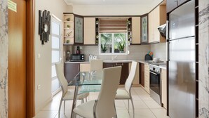Een moderne keuken met een glazen eettafel, roestvrijstalen apparatuur en uitzicht op de omgeving.