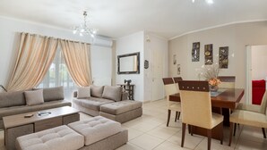 Een moderne woonkamer met een zithoek, een eettafel met stoelen en een kroonluchter.