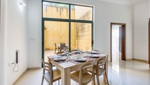 A dining area with a large window, a table set for four, and a view of a courtyard. - Relaxing Xaghra Apartment With BBQ Amenities (Xaghra)